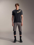 Alpinestars A-Dura Lipan Jersey met korte mouwen, zwart met grijs gemêleerde mouwen en zandkleurig Astars-logo op de borst, gedragen door een mannelijk model met een grijze mountainbikeshort en zwarte kniebeschermers, technische MTB-kleding