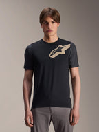 Mannelijk model draagt Alpinestars A-Dura Lipan jersey met korte mouwen, zwart MTB mountainbike-jersey met beige sterlogo en donkergrijze mouwen, gecombineerd met een grijze fietsbroek, casual sportkleding
