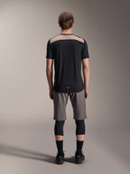 Alpinestars A-Dura Lipan Jersey - Korte mouwen, zwart met tan bovenpaneel op de rug, achteraanzicht met verlengde achterkant, gedragen met grijze MTB-short en zwarte kniebeschermers, technische mountainbikekleding