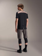 Alpinestars A-Dura Lipan Jersey met korte mouwen in het zwart, achteraanzicht op model met het lichtbruine geperforeerde mesh-paneel op de bovenrug, gecombineerd met een grijze mountainbikebroek en zwarte kniebeschermers voor een complete trail-rijoutfit.