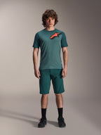 Alpinestars A-Dura Lipan Jersey, MTB-shirt met korte mouwen, Silver Pine groen met zwart en oranje Astars-logo op de borst, gecombineerd met bijpassende shorts en zwarte schoenen, technische mountainbikekleding