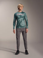 Alpinestars A-Dura Hollow Camo jersey met lange mouwen, Silver Pine Camo met groen camouflagepatroon, groot wit "astars" logo op de borst, gedragen met grijze technische broek en zwarte fietsschoenen, hoogwaardige MTB-uitrusting