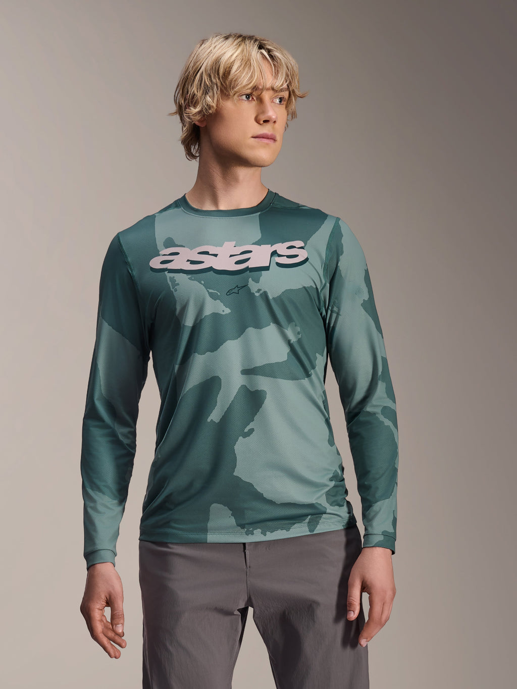 Alpinestars A-Dura Hollow Camo Jersey met lange mouwen, MTB-shirt, groen camouflagepatroon in Silver Pine Camo, groot lichtgrijs astars-logo op de borst, gedragen met een grijze broek, hoogwaardige mountainbikekleding