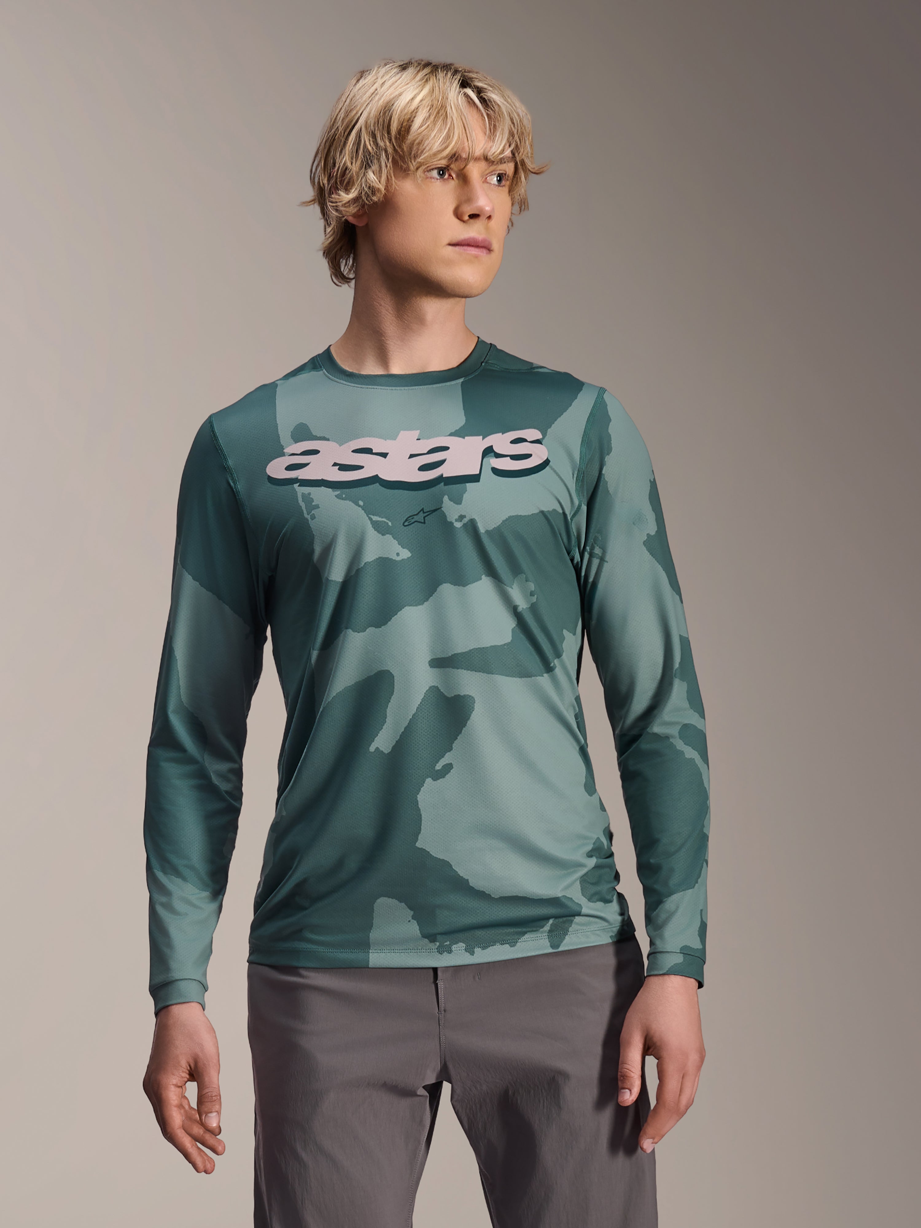 Alpinestars A-Dura Hollow Camo Jersey met lange mouwen, MTB-shirt, groen camouflagepatroon in Silver Pine Camo, groot lichtgrijs astars-logo op de borst, gedragen met een grijze broek, hoogwaardige mountainbikekleding