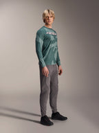 Alpinestars A-Dura Hollow Camo Jersey met lange mouwen, Silver Pine Camo, gedragen door een model met een grijze broek en zwarte schoenen, voorzien van een groen camouflagepatroon en een opvallend wit ASTARS-logo op de borst, hoogwaardige MTB-kleding