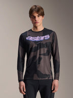 Alpinestars A-Dura Hollow Camo jersey met lange mouwen, MTB mountainbike-shirt, zwart en grijs camouflagepatroon, paarse 'astars' graphic op de borst, gedragen door model met zwarte broek, casual performance-ontwerp