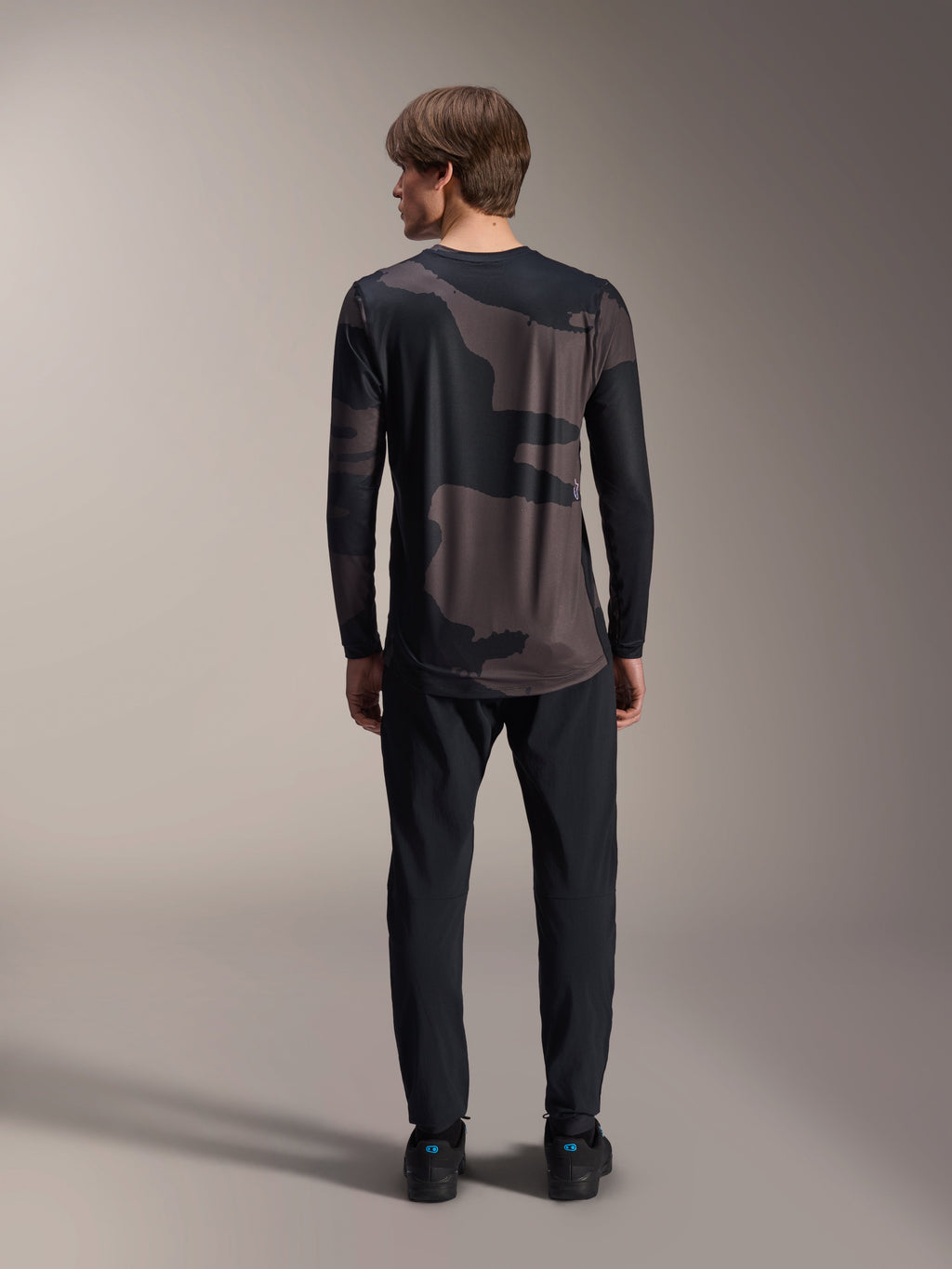 Alpinestars A-Dura Hollow Camo Jersey met lange mouwen, Black Camo, achteraanzicht gedragen met een zwarte broek, voorzien van een donker camouflagepatroon en een verlengde achterkant voor MTB-dekking.