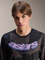 Alpinestars A-Dura Hollow Camo Jersey met lange mouwen, Black Camo met paarse 'astars' grafische opdruk op de borst, studiofoto van een mannelijk model in MTB-kleding, casual en technische mountainbikestijl