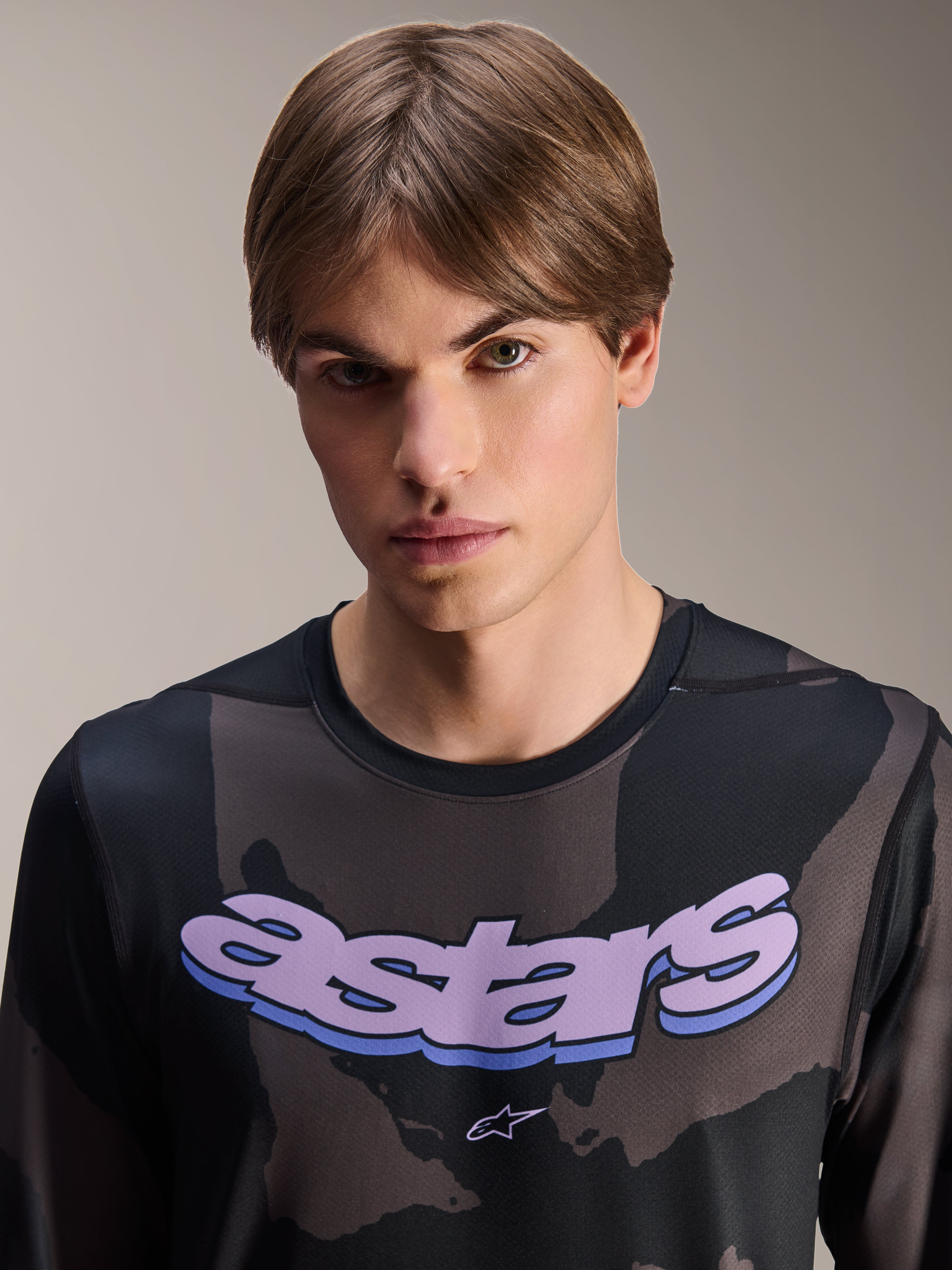 Alpinestars A-Dura Hollow Camo Jersey met lange mouwen, Black Camo met paarse 'astars' grafische opdruk op de borst, studiofoto van een mannelijk model in MTB-kleding, casual en technische mountainbikestijl