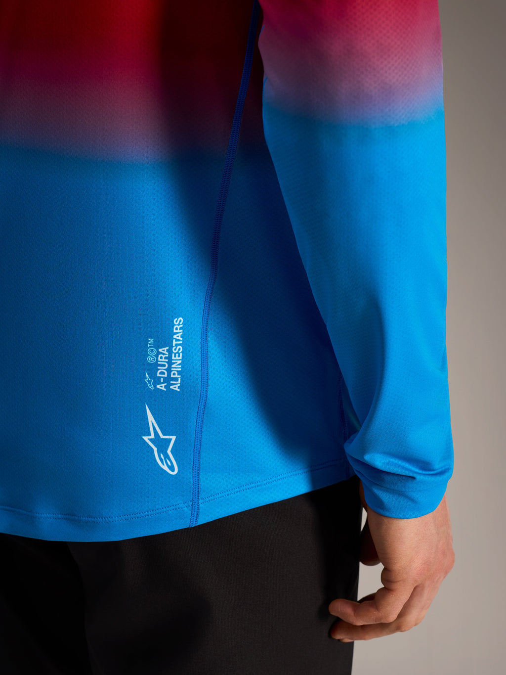 A-Dura ASTARS Jersey 2.0 met lange mouwen, rood-blauw kleurverloop en wit Alpinestars-logo op de zijkant.