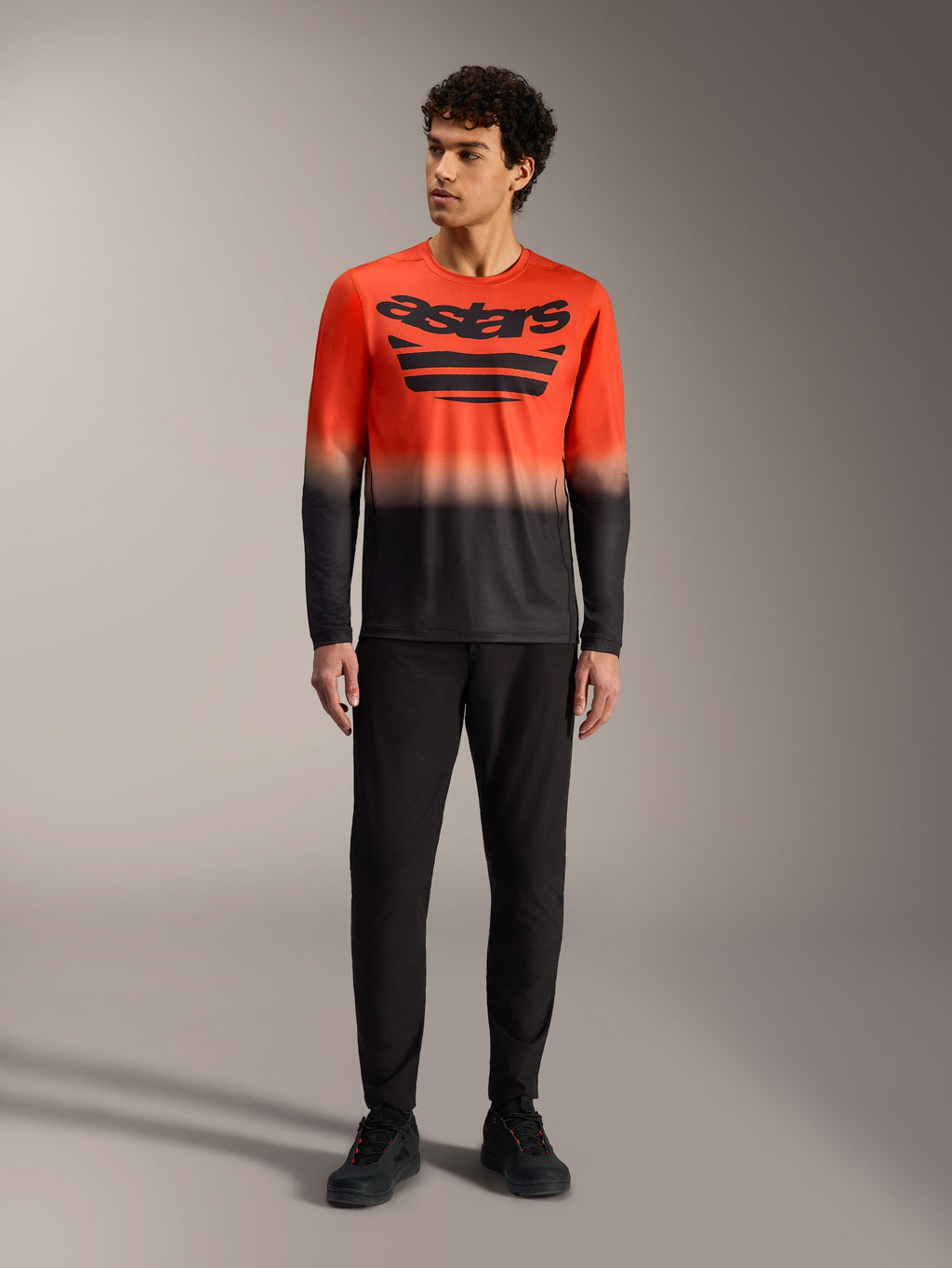 A-Dura ASTARS Jersey 2.0 met lange mouwen, oranje en zwart kleurverloop, groot borstlogo en zwarte MTB-broek.