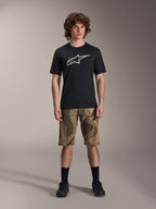 Alpinestars A-Dura Astar jersey met korte mouwen, zwart met groot wit Astars-logo op de borst, gedragen door een model met camouflage MTB-short en zwarte fietsschoenen, casual mountainbike-kleding