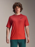 Alpinestars 2025 A-Dura Rise Jersey, MTB-shirt met korte mouwen, Spicy Orange, gedragen door een man, voorzien van een zwart Astars-logo op de borst, gecombineerd met een donkergroene broek, casual mountainbike-performancekleding