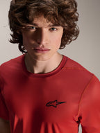 Close-up portret van een mannelijk model dat de Alpinestars A-Dura Rise Jersey met korte mouwen draagt in Spicy Orange, voorzien van een klein zwart Astars-logo op de borst, technische mountainbike kleding