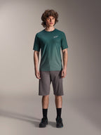 Mannelijk model draagt Alpinestars A-Dura Rise Jersey - Korte Mouwen in Silver Pine, groen fietsshirt met klein wit logo op de borst, gecombineerd met een grijze mountainbike short en zwart schoeisel, casual MTB-trailuitrusting