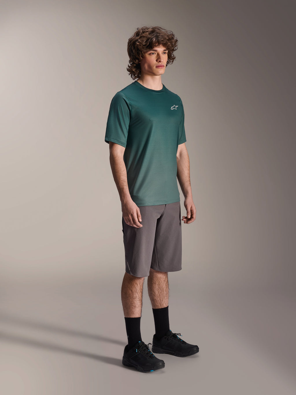 Alpinestars A-Dura Rise Jersey - Korte Mouwen in Silver Pine, groene mountainbike jersey gedragen door een model met grijze short en zwarte sneakers, casual MTB trail kleding met een klein wit logo op de borst