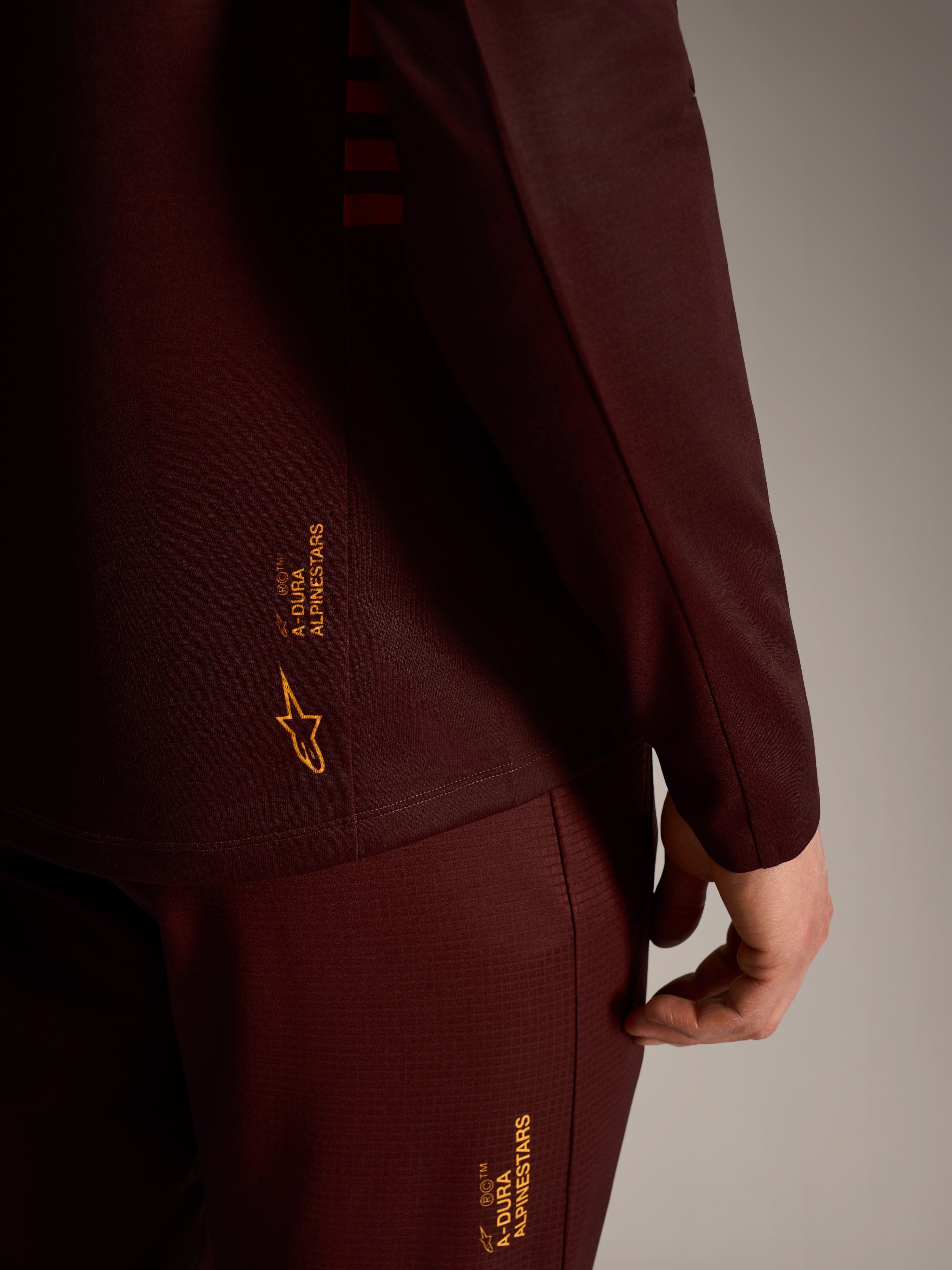 A-Dura Elite trui met lange mouwen in bordeaux, met gele Alpinestars-branding, technische trail-prestatiekleding.