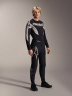 Mannelijk model draagt Alpinestars A-Supra Melt Jersey met lange mouwen, zwart met grijze grafische accenten, 'astars' logo op de borst, gecombineerd met bijpassende zwarte broek en schoenen, performance mountainbike-uitrusting voor off-road racen
