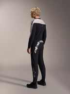 Alpinestars A-Supra Melt broek, MTB-broek, zwart, voorzien van een groot wit Alpinestars-woordmerk op de achterpas en een sterlogo op de broekspijp, gedragen door een model met een bijpassende jersey met lange mouwen en zwarte schoenen, zij-achteraanzicht