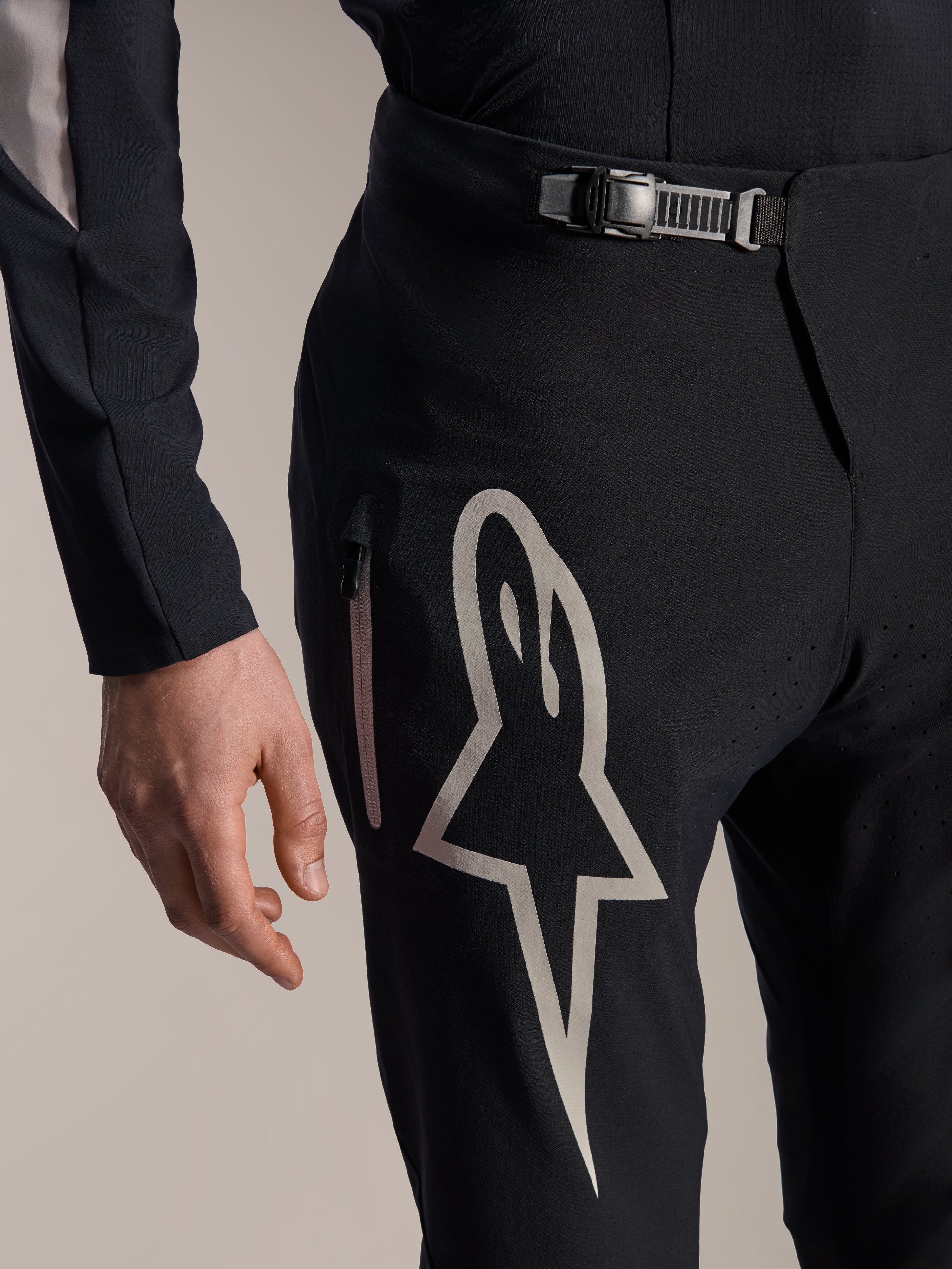 Alpinestars A-Supra Melt broek, mountainbikebroek, zwart, voorzien van een groot wit Astar-logo op de dij, verstelbare ratelsluiting en zijzak met rits, detailweergave van technische MTB-uitrusting