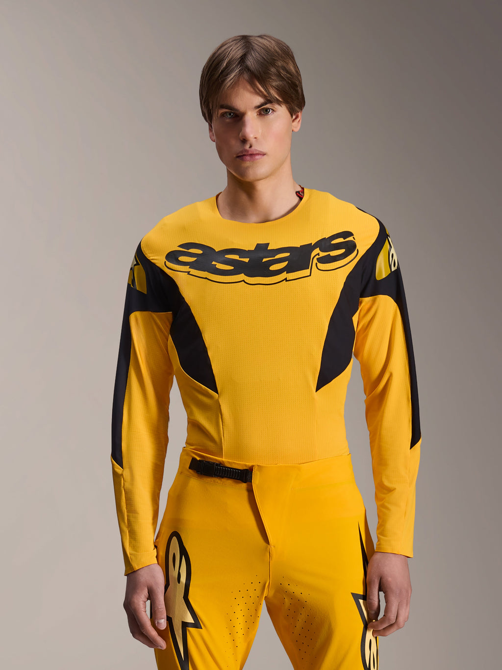 Alpinestars Limited Edition A-Supra Melt Gold Jersey, MTB-jersey met lange mouwen, donkergeel met zwarte accenten, gedragen door een model met bijpassende broek, voorzien van een groot zwart 'astars'-logo op de borst en een sportief prestatiegericht ontwerp