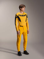 Model draagt Alpinestars Limited Edition A-Supra Melt Gold Jersey, MTB-jersey met lange mouwen in donkergeel en zwart, gecombineerd met bijpassende gele broek en zwarte schoenen, technische off-road fietskleding met racing-geïnspireerde graphics