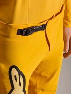 Alpinestars Limited Edition A-Supra Melt Gold broek, mountainbikebroek, donkergeel, close-up van de zwarte ratelsluiting aan de tailleband, voorzien van laserperforaties op de binnenzijde van het dijbeen voor ventilatie