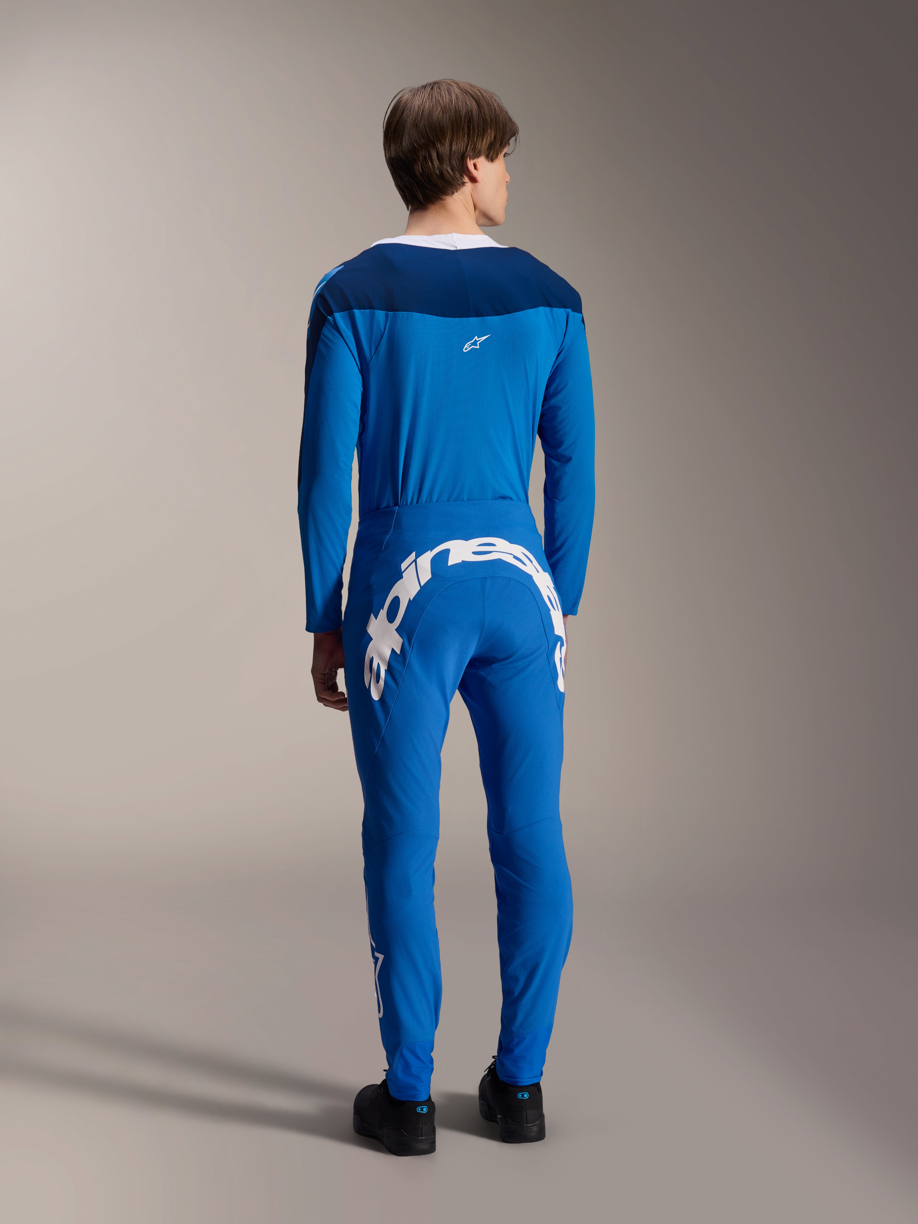 Mannelijk model van achteren gezien in de Alpinestars A-Supra Melt Jersey met lange mouwen in het blauw, gecombineerd met een bijpassende blauwe performance broek met een groot wit Alpinestars-woordmerk op de achterkant, complete MTB-racekit.