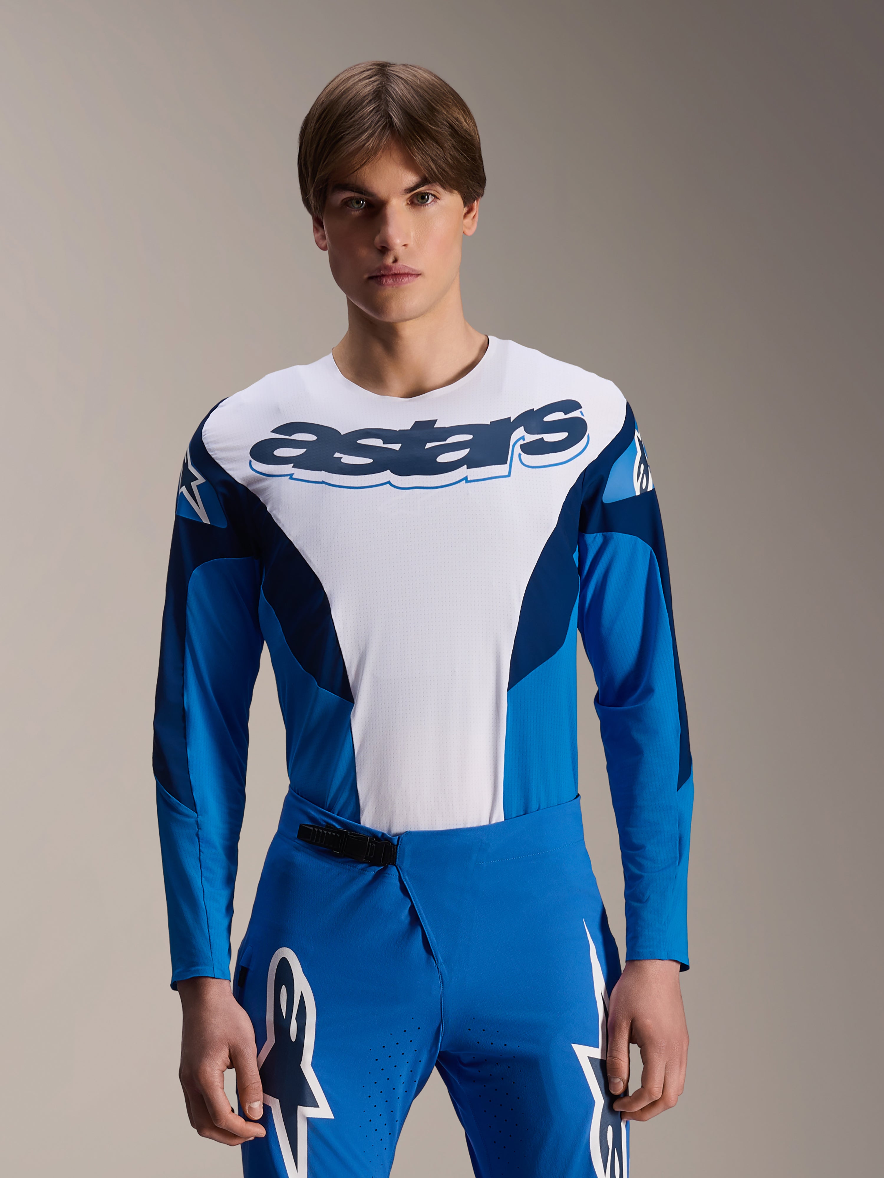 Alpinestars A-Supra Melt Jersey met lange mouwen, blauw en wit MTB-shirt met opvallende astars-branding op de borst en donkerblauwe mouwen, gedragen met bijpassende blauwe racebroek met witte sterlogo's, hoogwaardige mountainbike-kleding