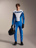 Mannelijk model in Alpinestars A-Supra Melt MTB-kit, wit en blauw jersey met lange mouwen en 'astars' woordmerk, blauwe A-Supra Melt broek met wit logo, zwarte full-face helm, zwarte handschoenen en schoenen, gecoördineerde off-road wieleroutfit
