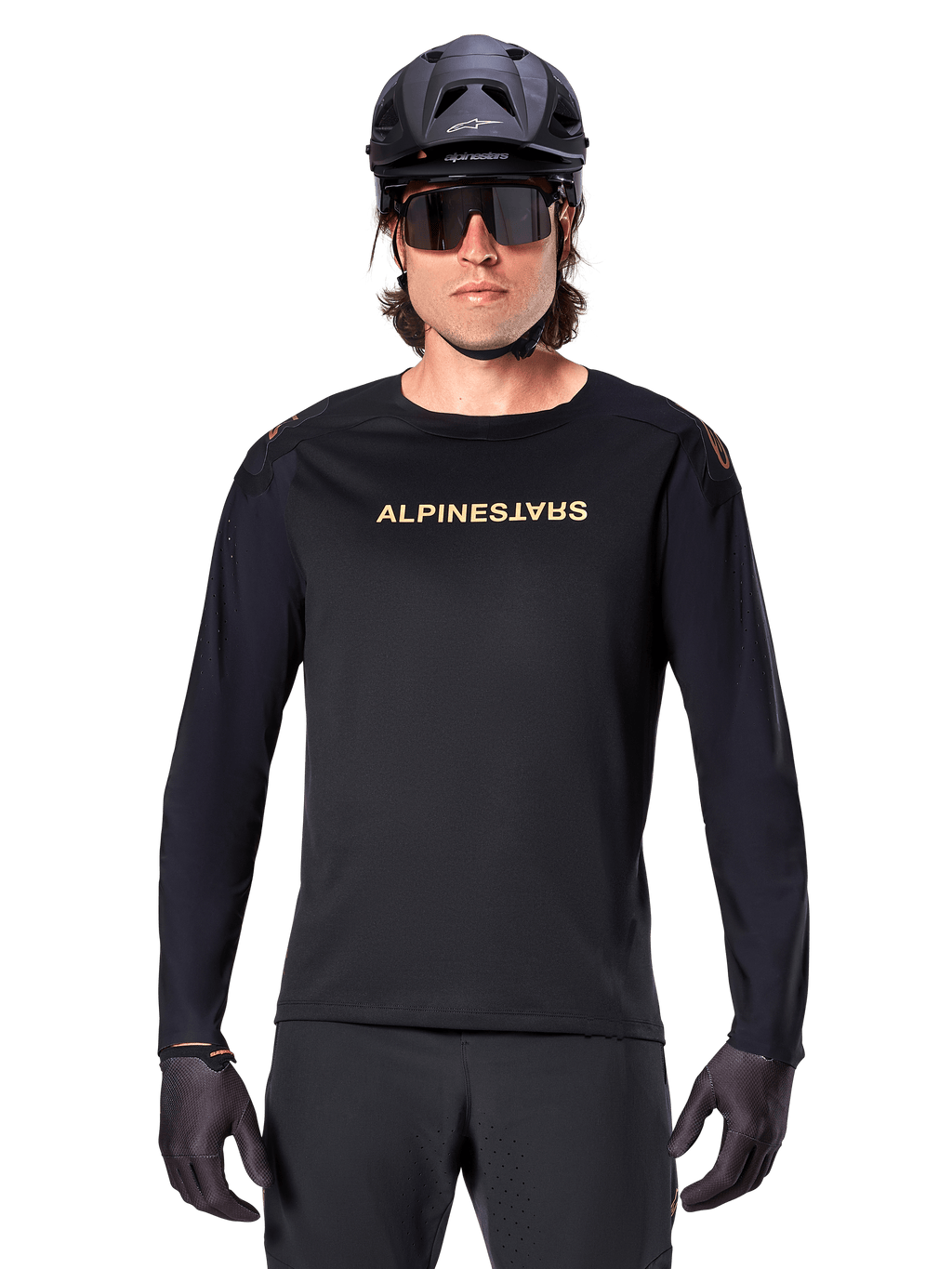 Alpinestars A-Aria Polartec Switch Jersey met lange mouwen, zwart, goudkleurig Alpinestars-logo op de borst, gedragen met een zwarte MTB-helm, donkere zonnebril en zwarte handschoenen, professionele mountainbike trailuitrusting