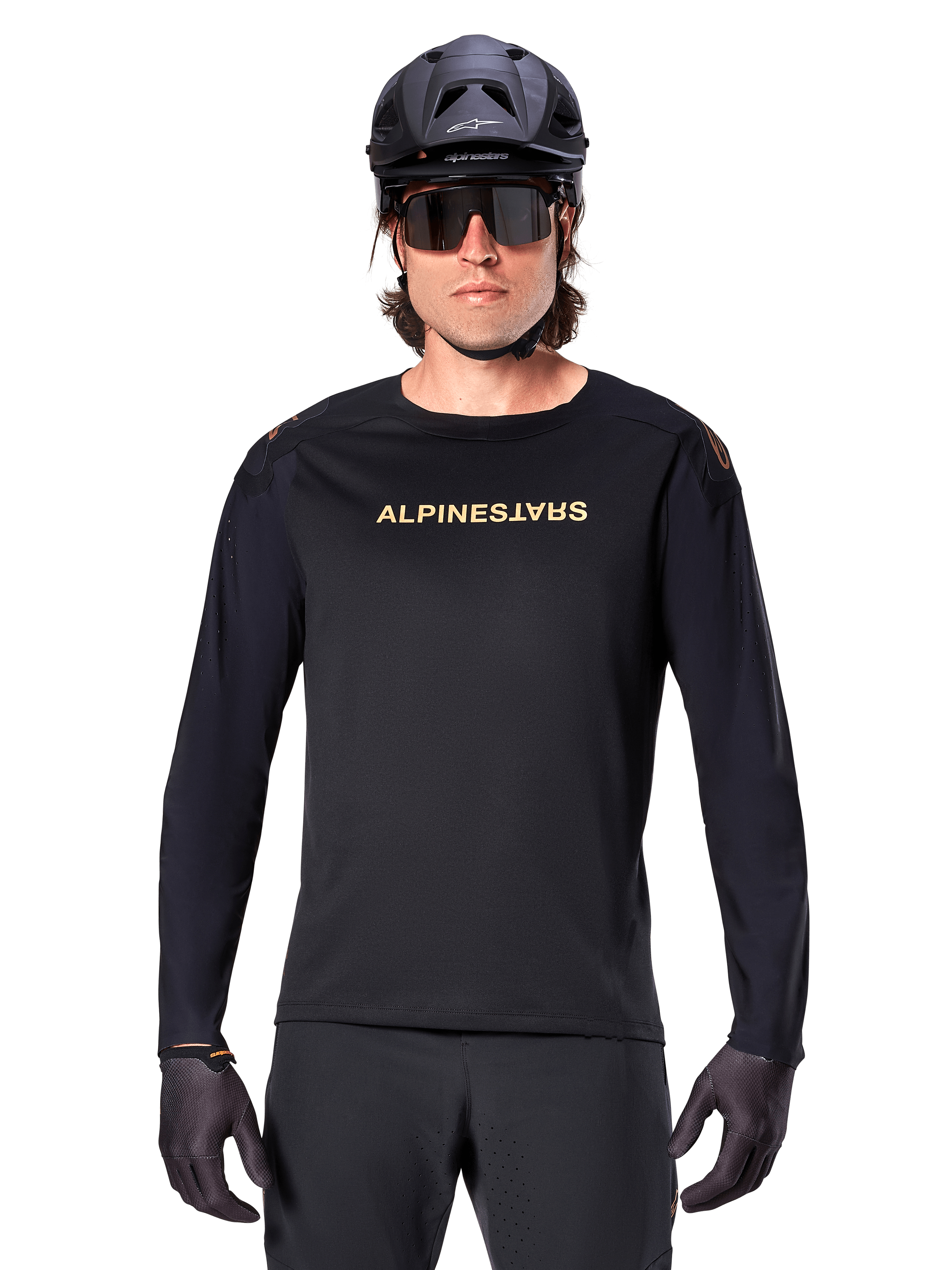 Alpinestars A-Aria Polartec Switch Jersey met lange mouwen, zwart, goudkleurig Alpinestars-logo op de borst, gedragen met een zwarte MTB-helm, donkere zonnebril en zwarte handschoenen, professionele mountainbike trailuitrusting