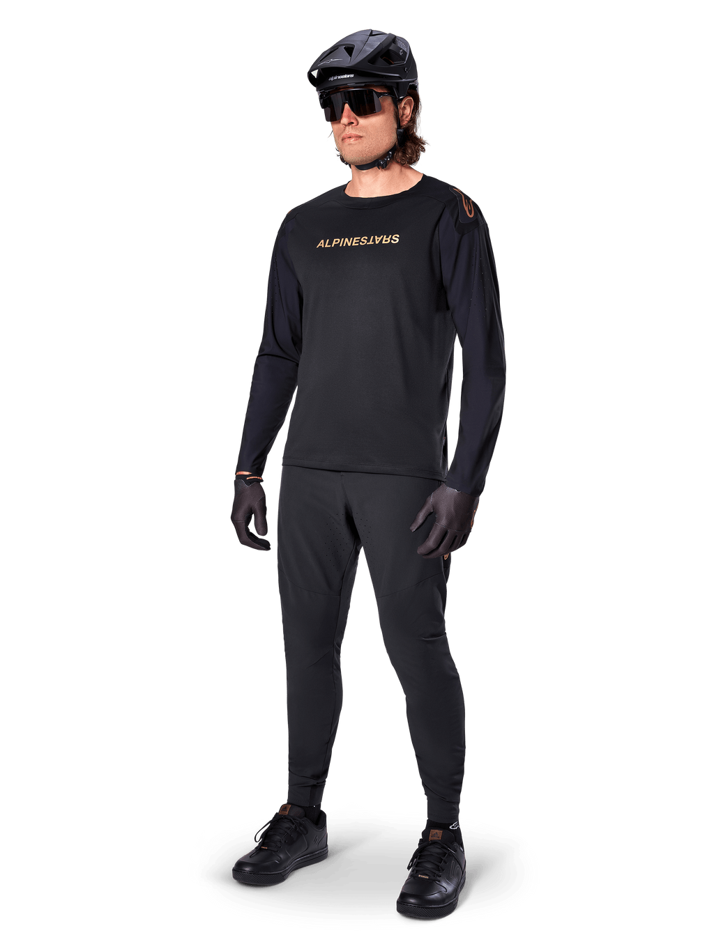 Alpinestars A-Aria Polartec Switch jersey met lange mouwen, zwart, bronskleurige branding op de borst, gedragen door mountainbiker met zwarte helm en zonnebril, hoogwaardige fietskleding voor trailrijden