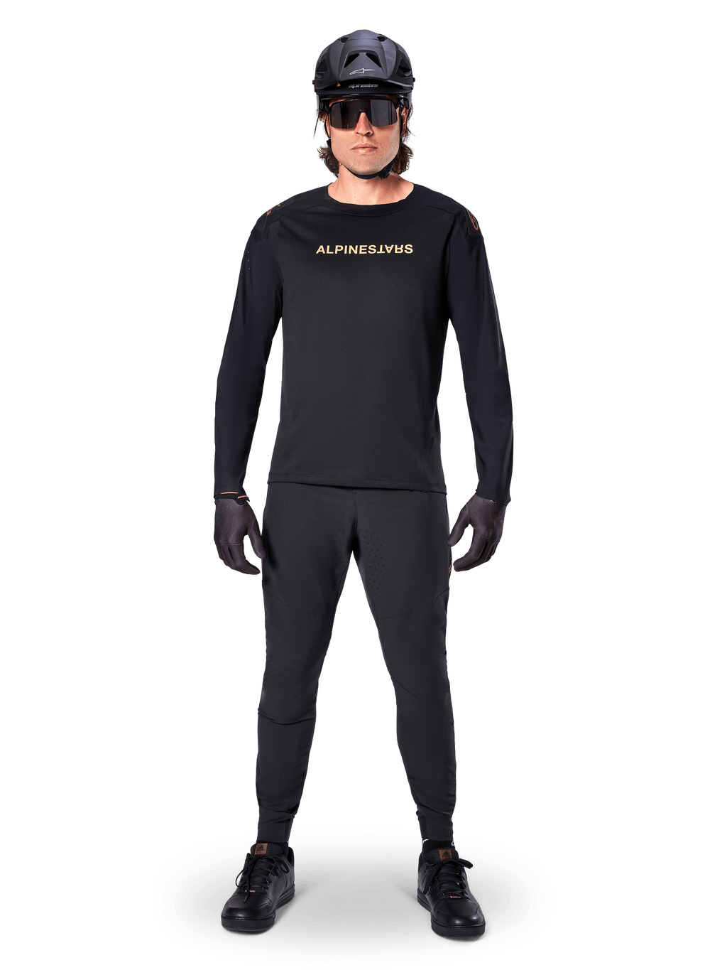 Alpinestars A-Aria Polartec Switch Jersey met lange mouwen, zwart, gedragen door een rijder met bijpassende zwarte technische broek, zwarte helm, zonnebril en zwarte handschoenen, performance MTB-uitrusting voor off-road paden