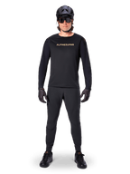 Alpinestars A-Aria Polartec Switch Jersey met lange mouwen, zwart, gedragen door een rijder met bijpassende zwarte technische broek, zwarte helm, zonnebril en zwarte handschoenen, performance MTB-uitrusting voor off-road paden