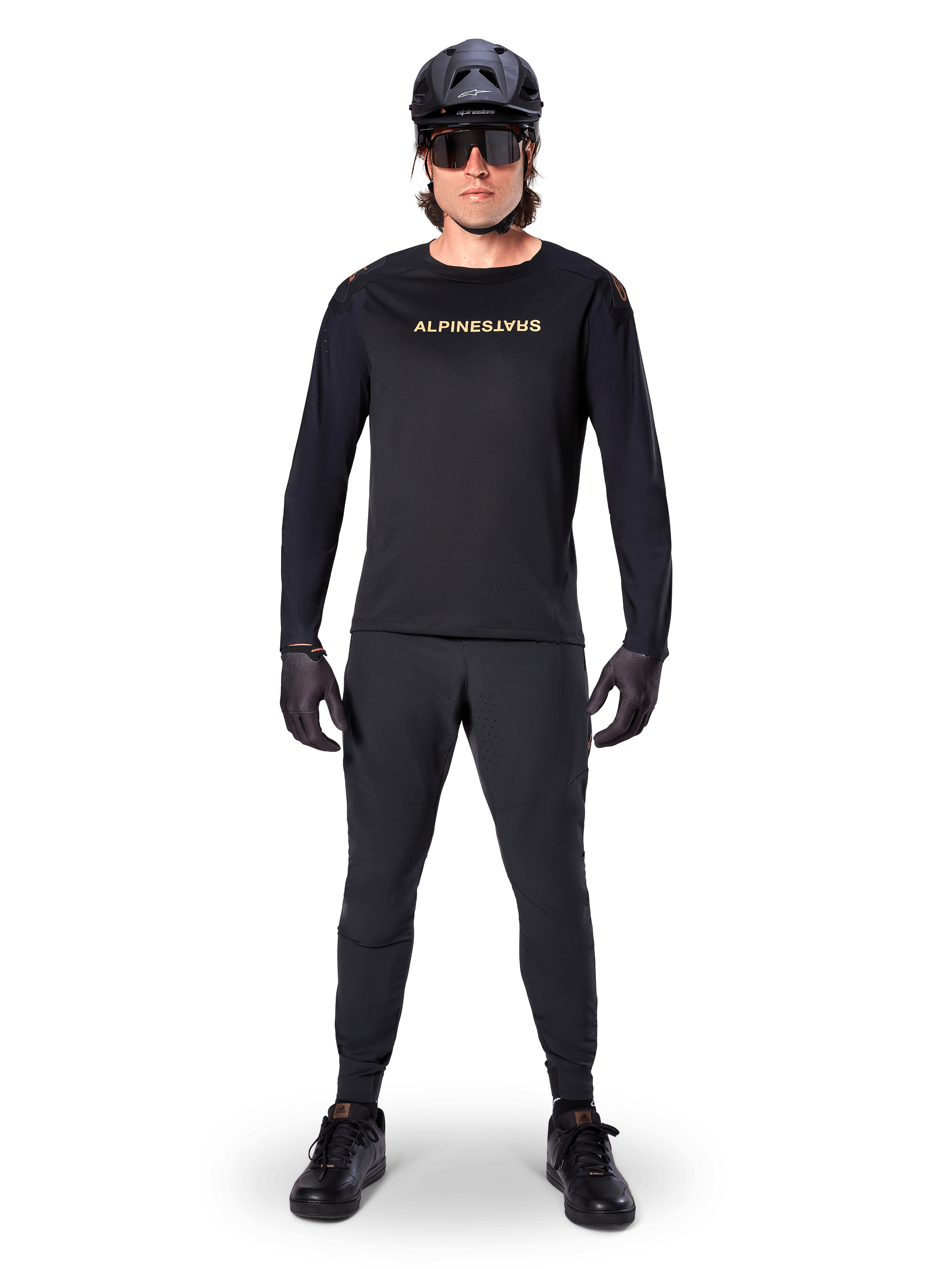 Alpinestars A-Aria Polartec Switch Jersey met lange mouwen, zwart, gedragen door een rijder met bijpassende zwarte technische broek, zwarte helm, zonnebril en zwarte handschoenen, performance MTB-uitrusting voor off-road paden