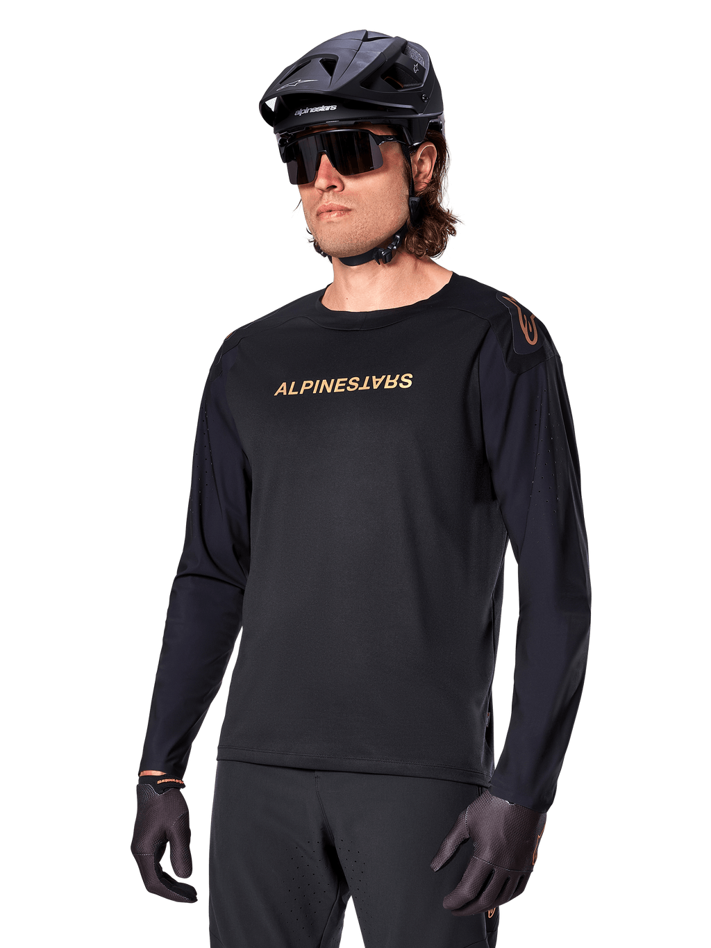 Alpinestars A-Aria Polartec Switch fietsshirt met lange mouwen, zwart met goudkleurig logo, MTB mountainbike-kleding, gedragen met een zwarte helm en zonnebril, met lasergesneden ventilatie op de mouwen en vochtafvoerende Polartec-stof voor off-road prestaties