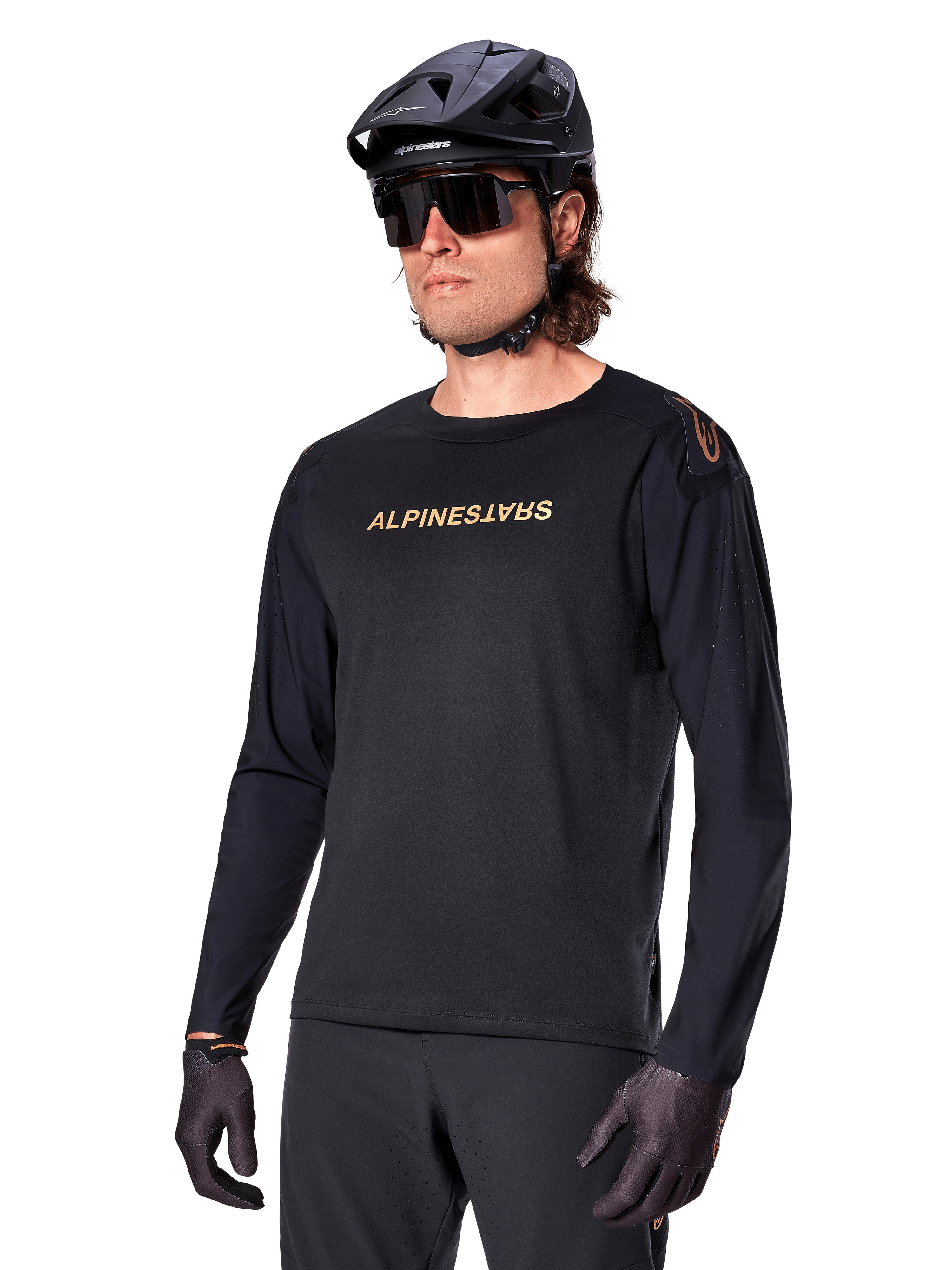 Alpinestars A-Aria Polartec Switch fietsshirt met lange mouwen, zwart met goudkleurig logo, MTB mountainbike-kleding, gedragen met een zwarte helm en zonnebril, met lasergesneden ventilatie op de mouwen en vochtafvoerende Polartec-stof voor off-road prestaties