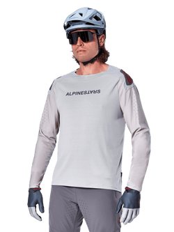 Alpinestars A-Aria Polartec Switch Jersey Long Sleeve, Light Gray cycling jersey with black chest logo and red shoulder accent, laser-perforated sleeves for airflow, worn with a light blue helmet, sunglasses, and gray pants, performance mountain bike apparel for trail riding