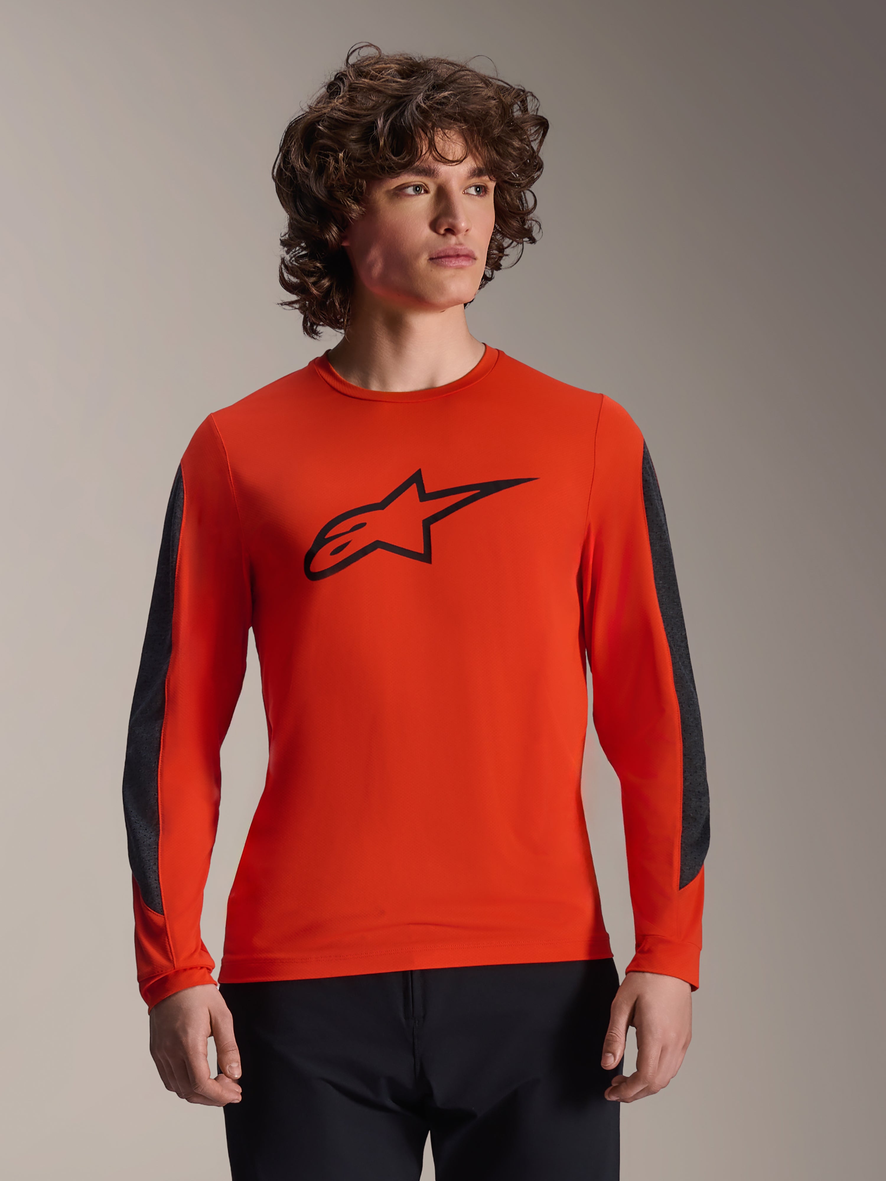 Alpinestars A-Dura Insert Astar Jersey met lange mouwen, Spicy Orange met zwart Astar-logo, voorzien van donkergrijze duurzame mouwinzetten, gedragen door een mannelijk model, performance MTB-fietskleding