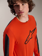 Alpinestars A-Dura Insert Astar Jersey met lange mouwen, Spicy Orange MTB-jersey met groot zwart Astar-logo op de borst, donkergrijze mouwpanelen, gedragen door een model in een close-up studio-opname, getextureerde technische stof.