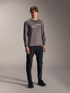 Alpinestars A-Dura Insert Astar Jersey, MTB-shirt met lange mouwen, donkergrijs, met groot wit logo op de borst, gedragen met zwarte technische broek en zwarte schoenen, off-road fietskleding