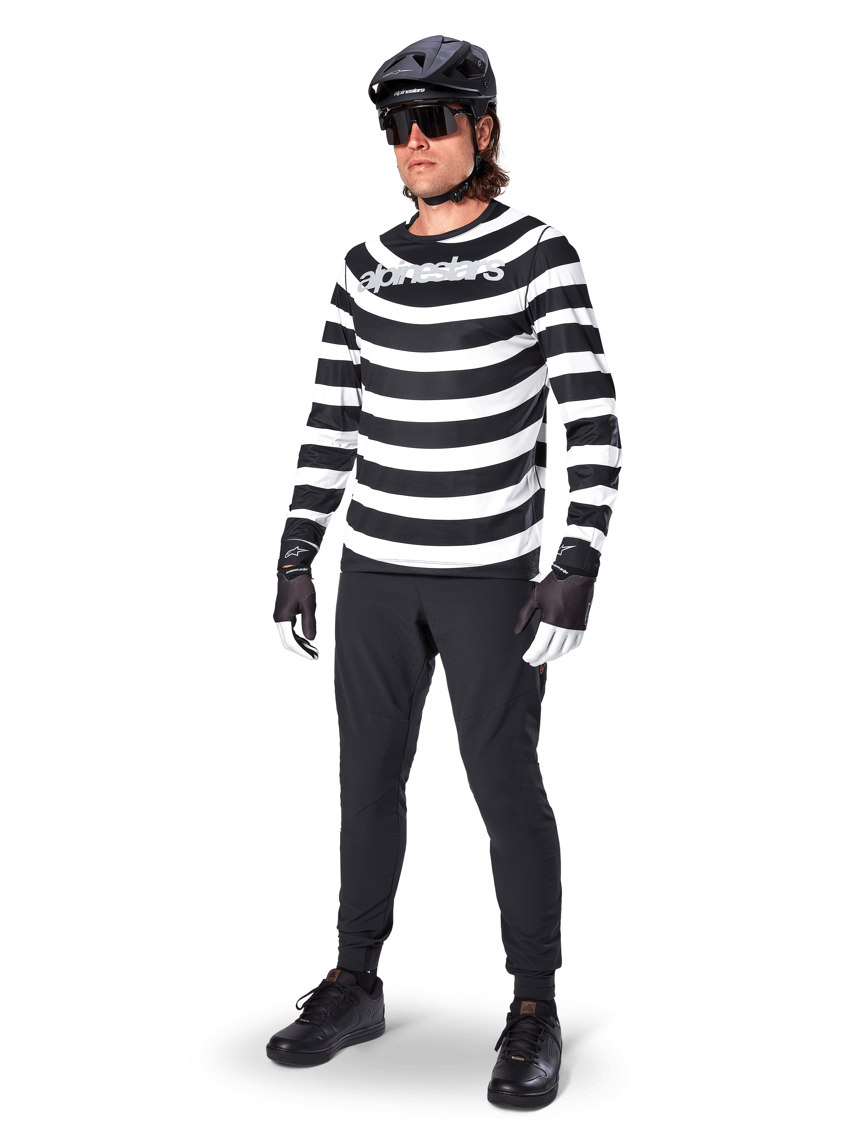 Alpinestars A-Aria Oscar Jersey met lange mouwen, zwart en wit met opvallende horizontale spiraalvormige strepen, wit gebogen Alpinestars-logo, performance MTB-kleding gedragen met zwarte fietsbroek en helm