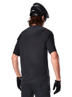 Alpinestars A-Aria Polartec Switch jersey met korte mouwen, zwart, achteraanzicht van een rijder met een zwarte mountainbikehelm, bijpassende zwarte short en handschoenen, performance kleding voor mountainbiken