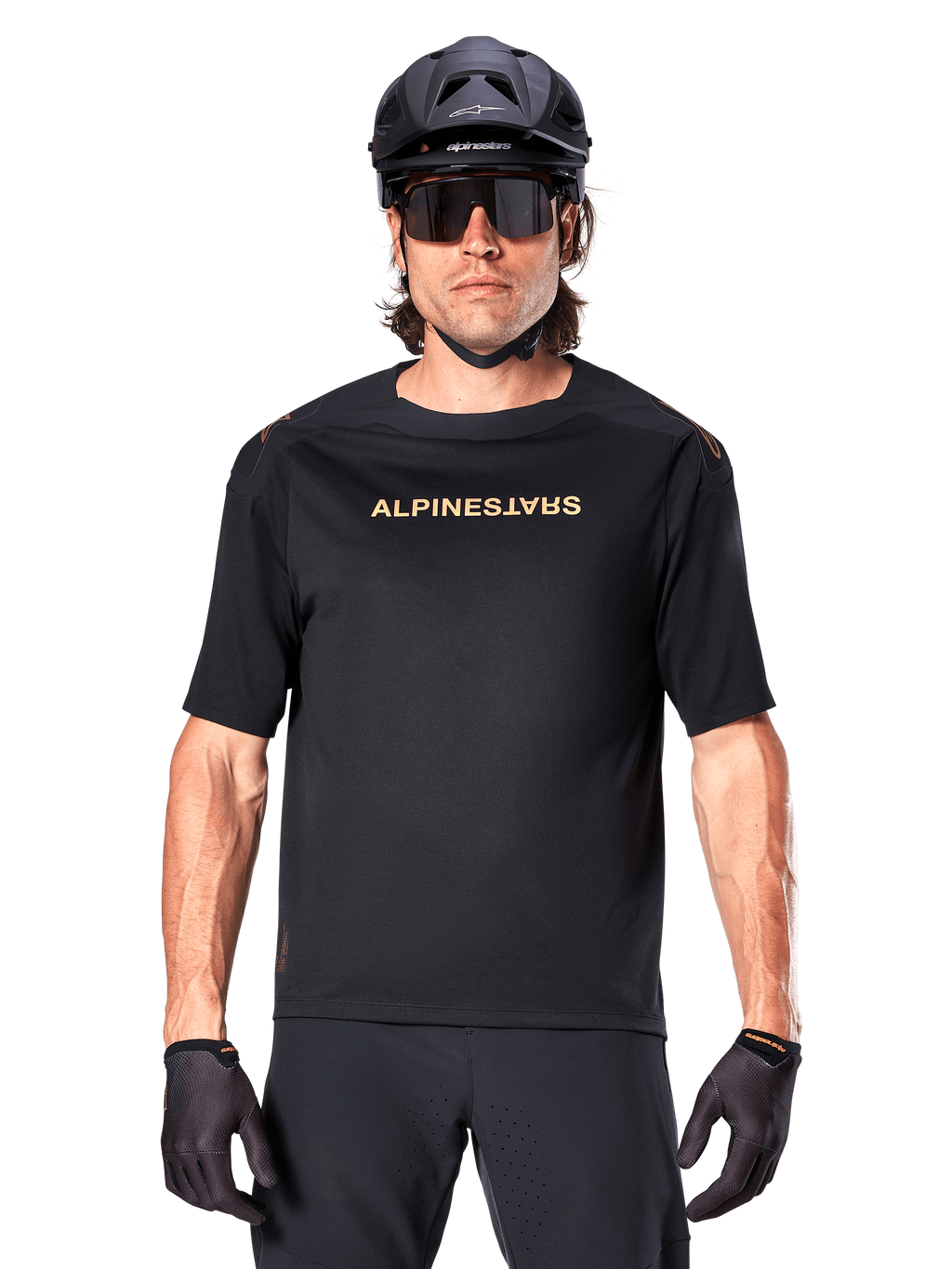 Alpinestars A-Aria Polartec Switch jersey met korte mouwen, zwart met goudkleurige branding op de borst, mountainbiker met zwarte MTB-helm, donkere sportzonnebril en bijpassende handschoenen, off-road fietskleding