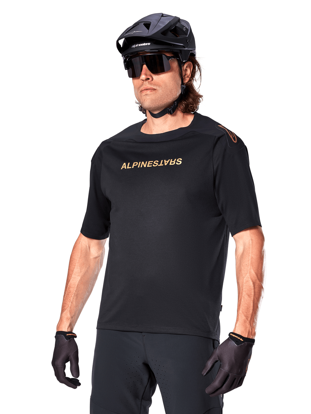 Alpinestars A-Aria Polartec Switch jersey met korte mouwen, zwart mountainbike-shirt met goudkleurige Alpinestars-branding, gedragen met zwarte helm, zonnebril en handschoenen, technische MTB-kleding