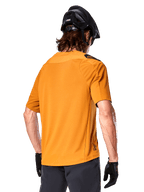 Alpinestars A-Aria Polartec Switch Jersey, Short Sleeve MTB Jersey, Dark Gold, back view showing performance fit, worn with black helmet and grey shorts, durable and breathable trail riding apparel