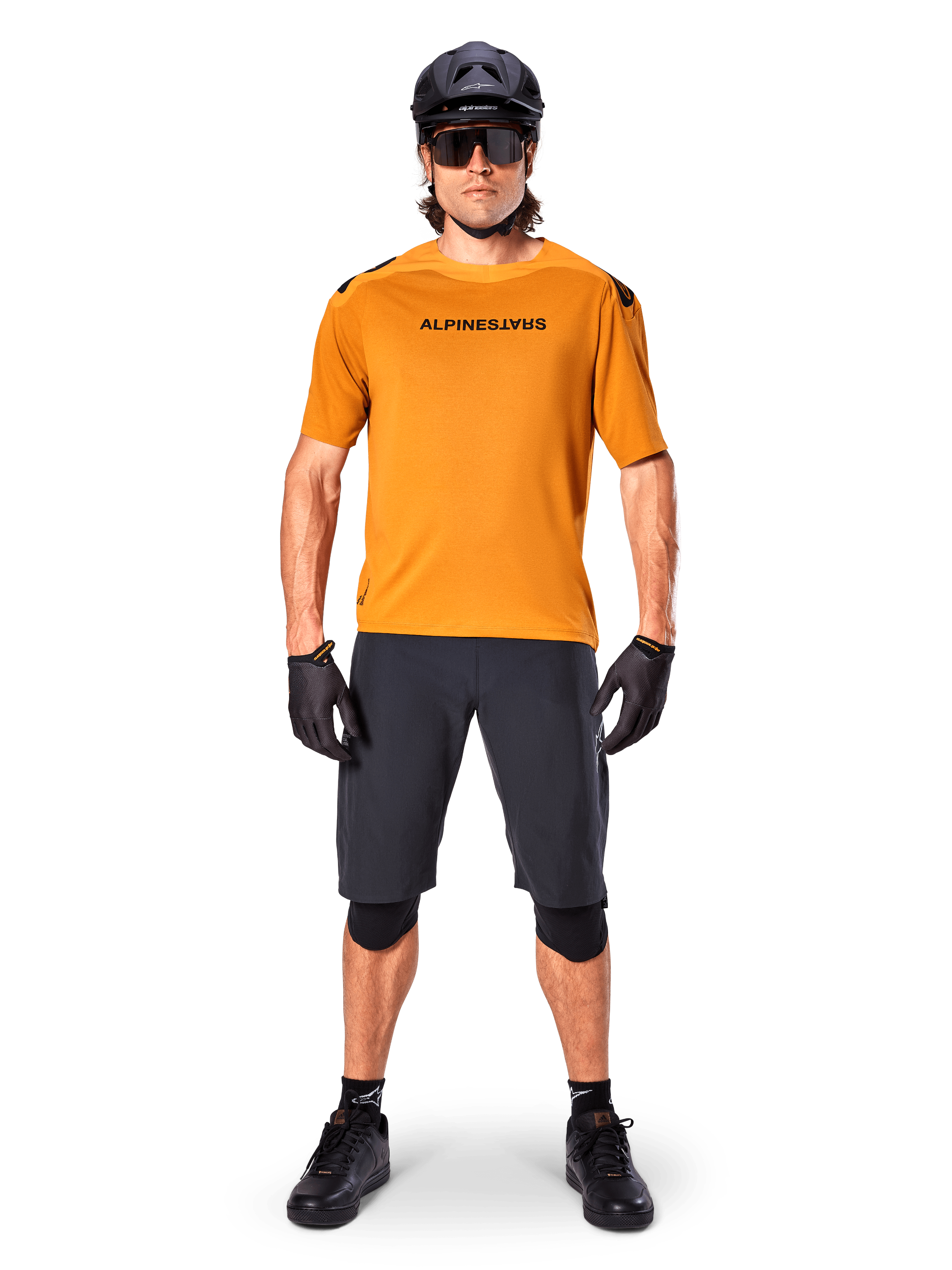 Male cyclist wearing the Alpinestars A-Aria Polartec Switch Short Sleeve Jersey in Dark Gold, paired with black MTB shorts, helmet, sunglasses, and gloves, professional mountain bike trail riding gear