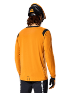 Alpinestars A-Dura Dri Wool Long Sleeve Jersey in Dark Gold, back view of a rider wearing a mountain bike helmet and gloves, featuring black mesh panels on the shoulders and a longer drop tail, technical cycling apparel for trail riding
