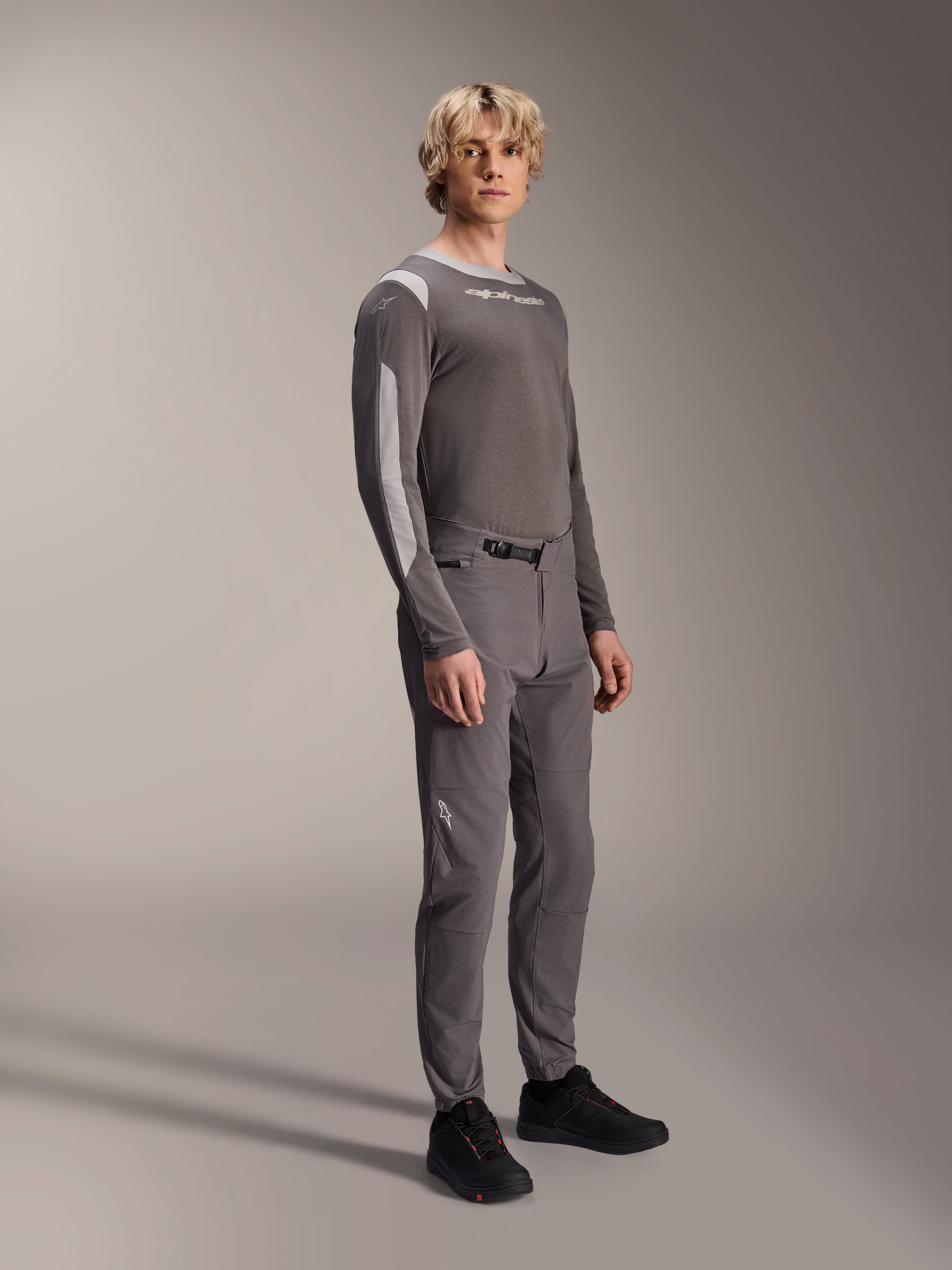 Alpinestars A-Dura Elite Pants, Mountain Bike Pants, Dark Gray, worn with a matching long-sleeve jersey and black shoes, featuring a front ratchet closure and durable Cordura fabric for trail and enduro riding